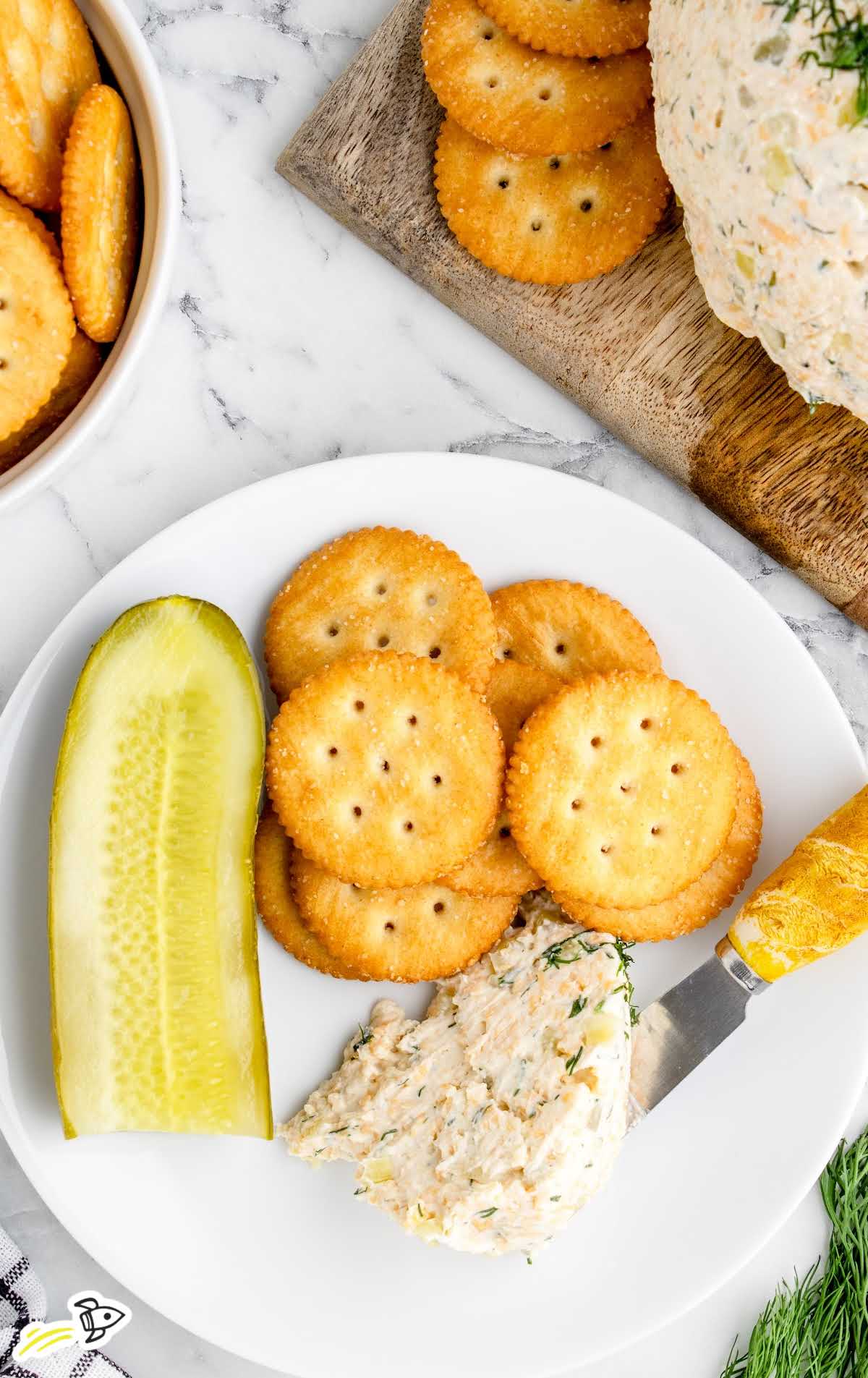 overhead shot of a piece of Dill Pickle Cheese Ball with crackers and a sliced pickle on a plate