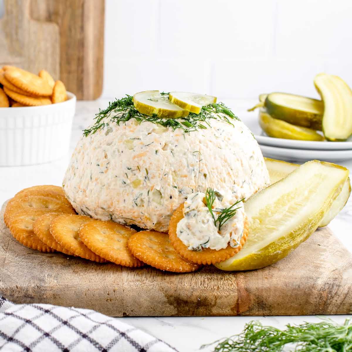 a close up shot of Dill Pickle Cheese Ball with crackers and a sliced pickle on a wooden board