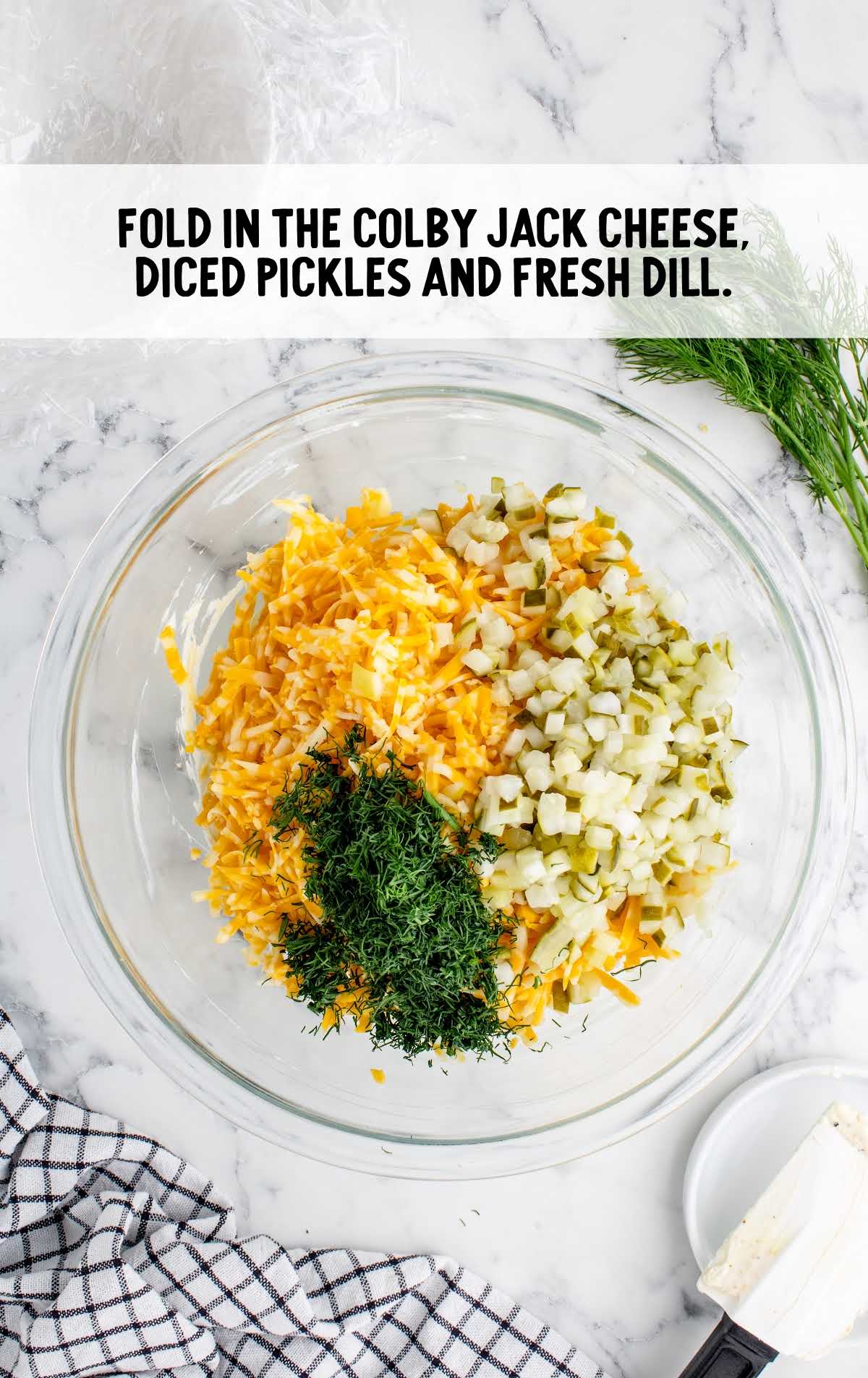 colby jack cheese, diced pickles and fresh dill folded in a bowl