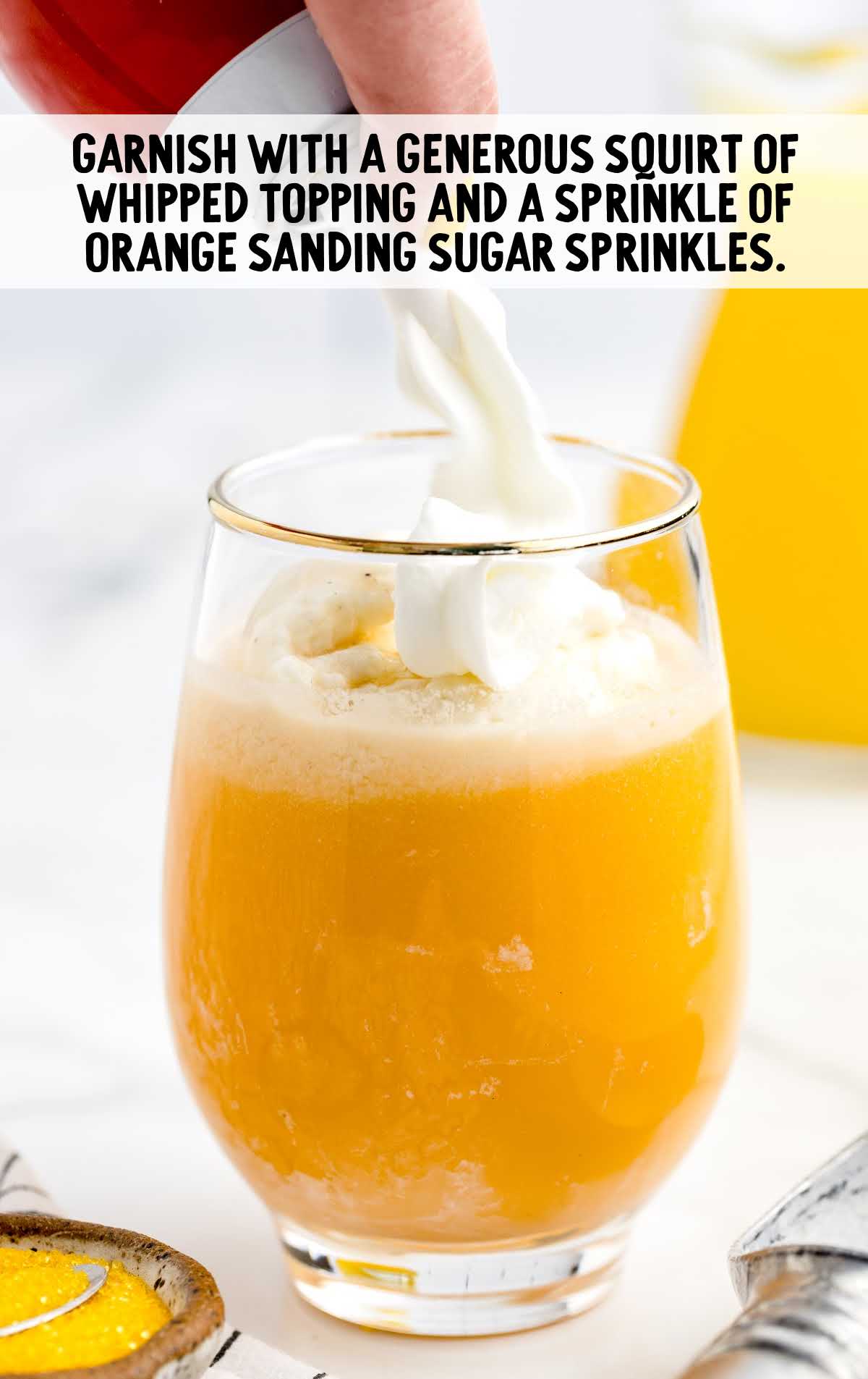 whipped topping garnished on top of the cocktail and orange sanding sugar sprinkled in a glass