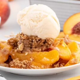 a close up shot of a slice of Peach Crisp on a plate topped with ice cream