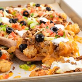 a close up shot of Tater Tot Nachos in a baking dish with a wooden spoon getting a piece