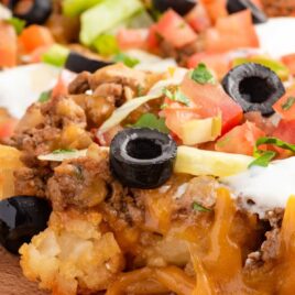 a close up shot of Tater Tot Nachos on a plate with a wooden spoon grabbing a spoon