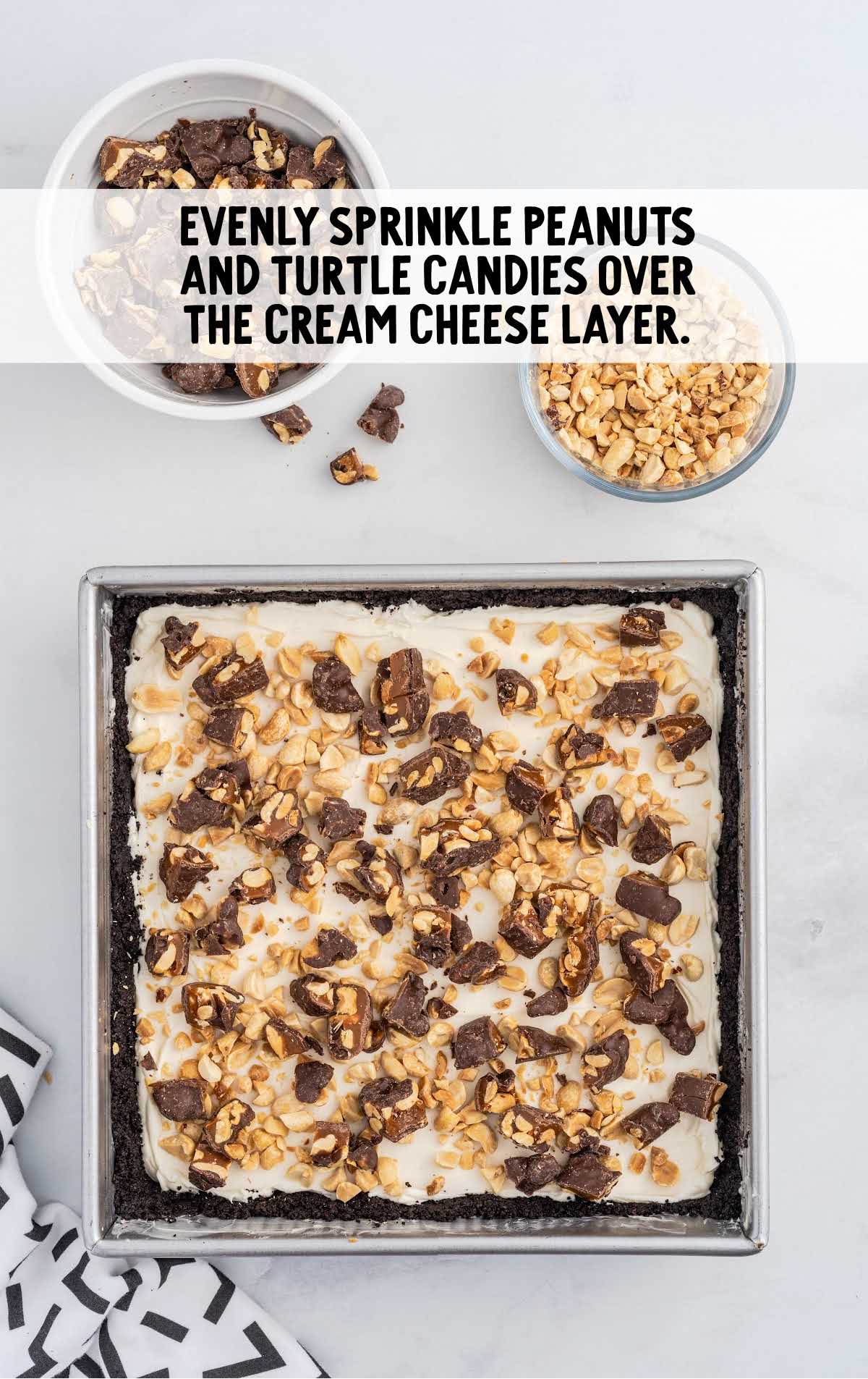 peanuts and turtle candies sprinkled over the cream cheese layer