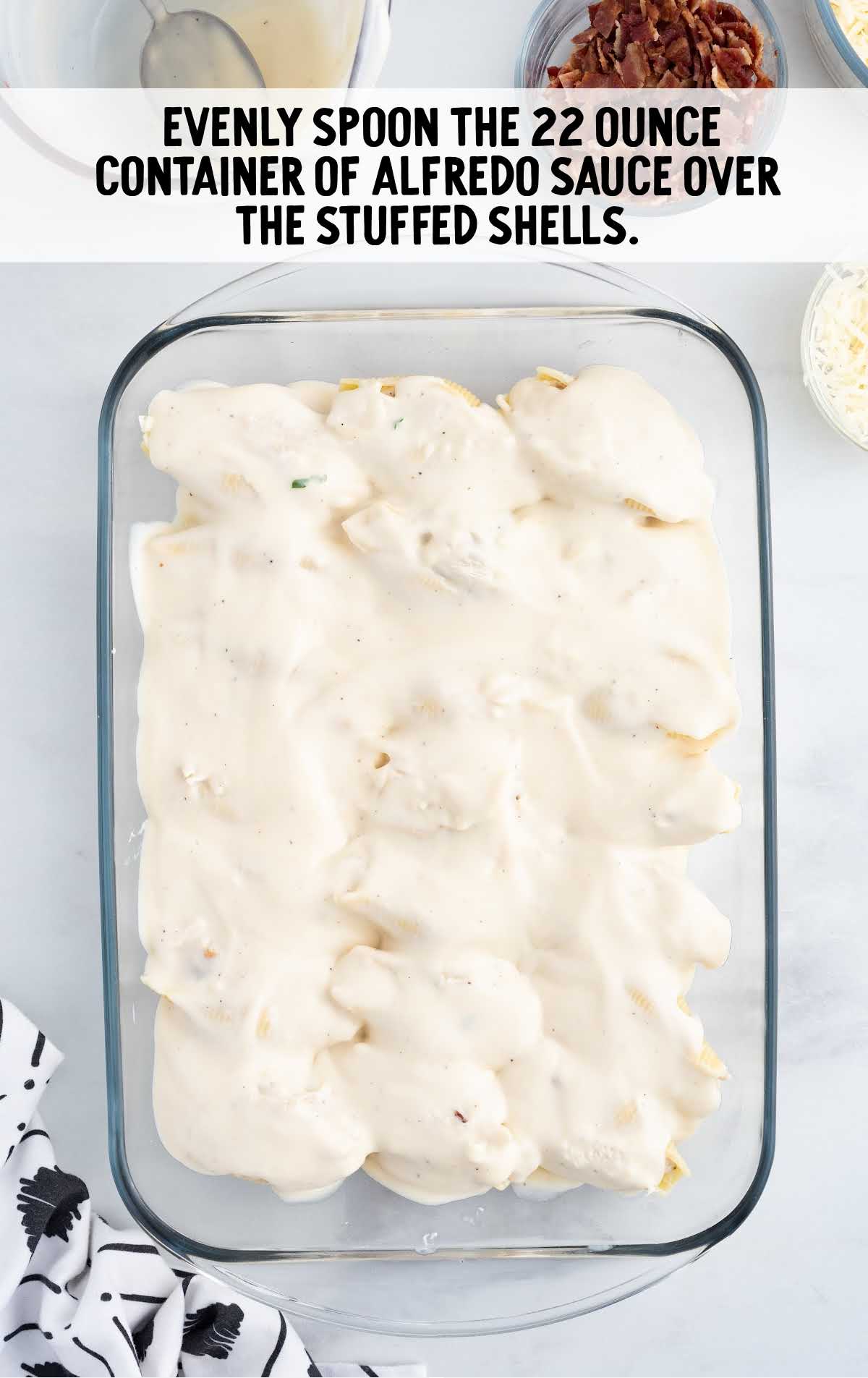 alfredo sauce spooned over the stuffed shell in a baking dish