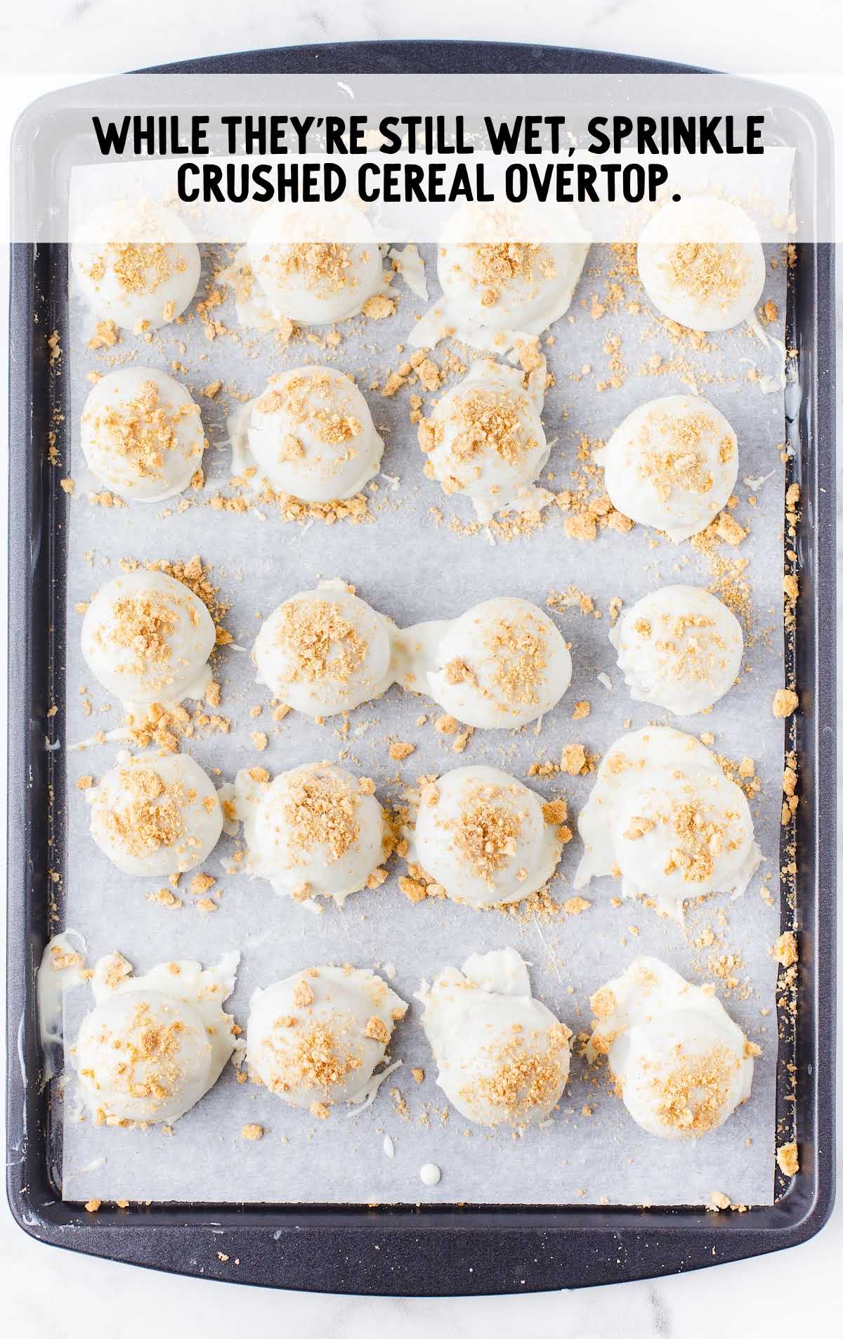 crushed cereal sprinkled over the top of the cheesecake bites on a baking sheet