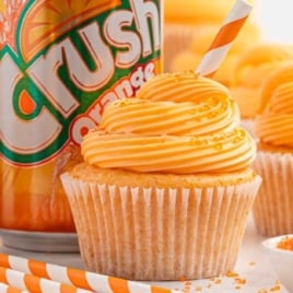 Close-up of a cupcake with orange frosting and a striped straw, with a can of Orange Crush soda in the background.