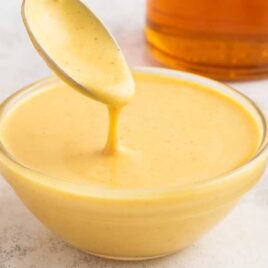 a close up shot of Honey Mustard Sauce in a bowl with a spoon full of sauce