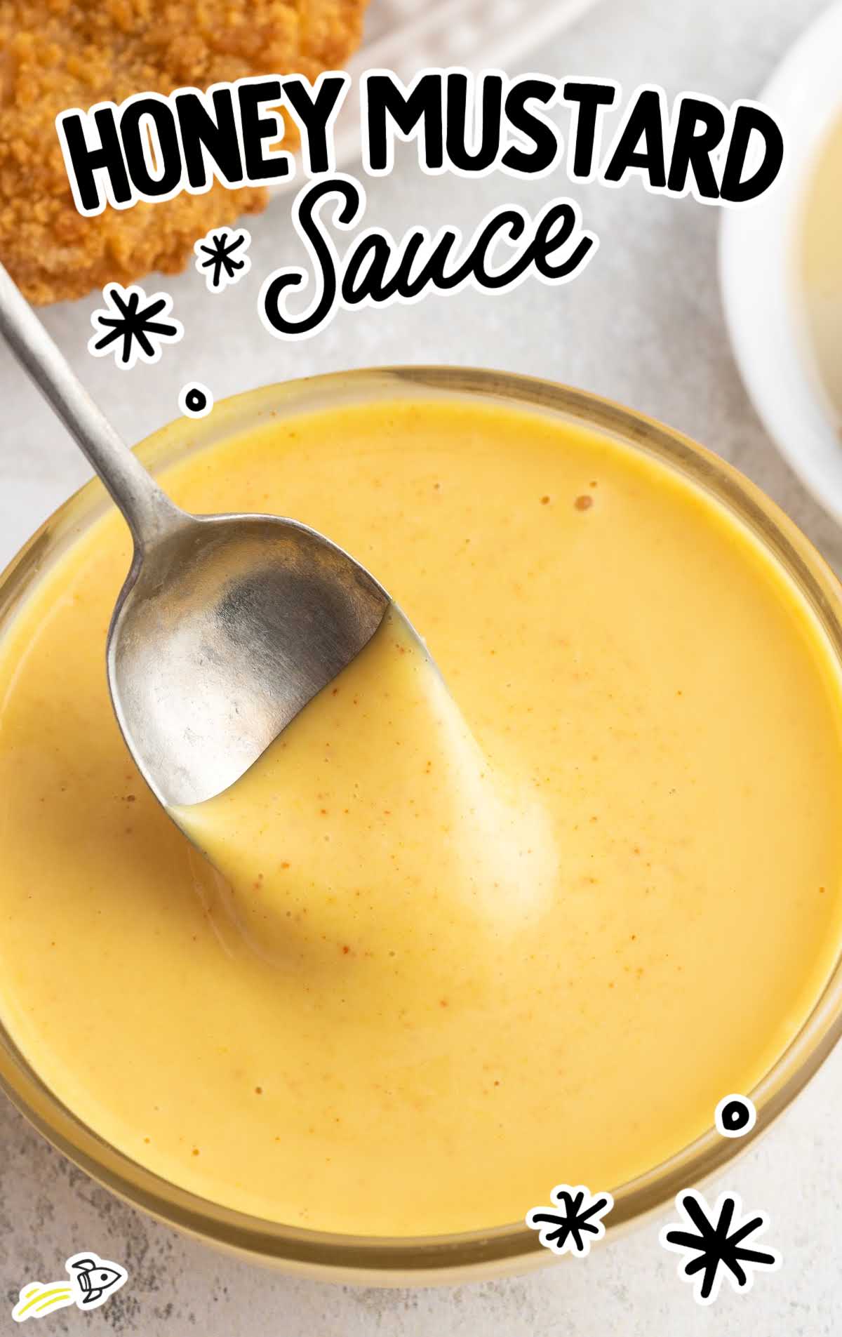 a close up shot of Honey Mustard Sauce in a bowl with a spoon full of sauce