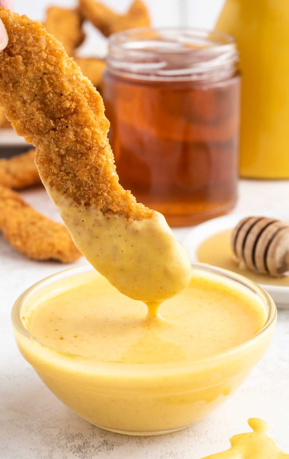 a close up shot of Honey Mustard Sauce in a bowl with a tender dipped in the sauce