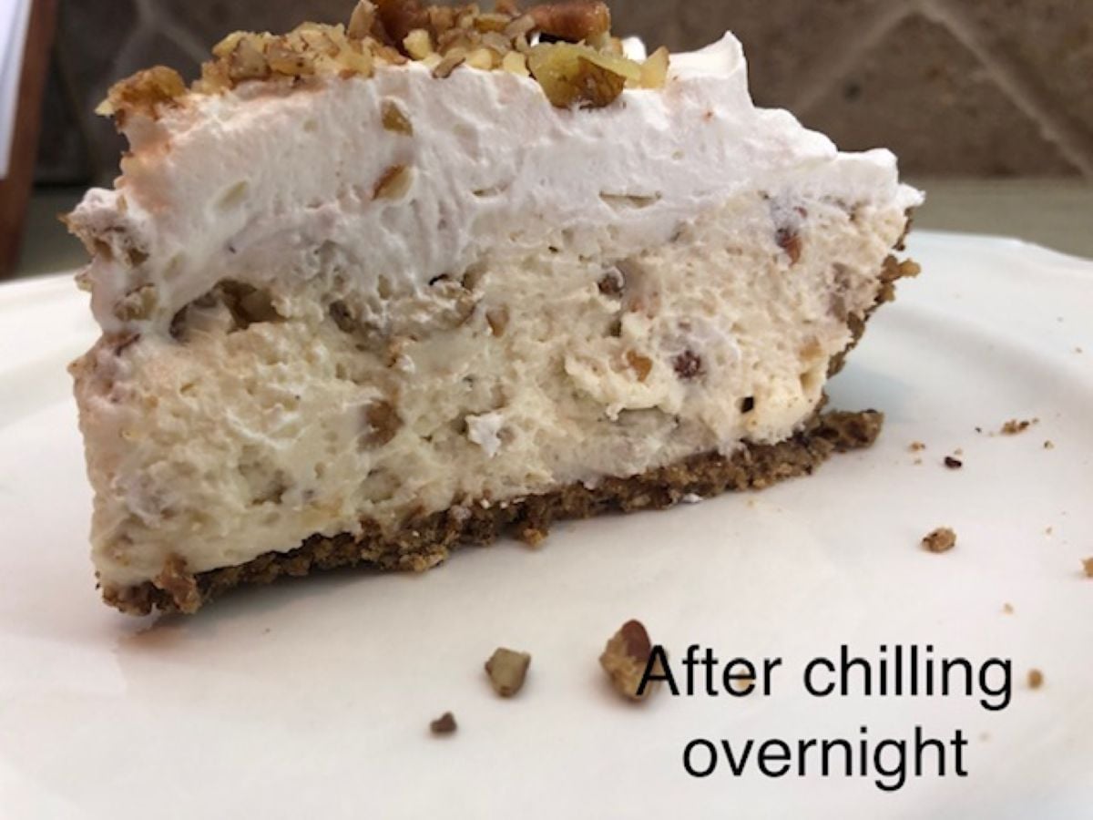 A slice of pecan cream pie with a nutty crust and whipped topping sits on a white plate. Chopped pecans are sprinkled on top and a few pieces rest on the plate. Text reads, After chilling overnight.