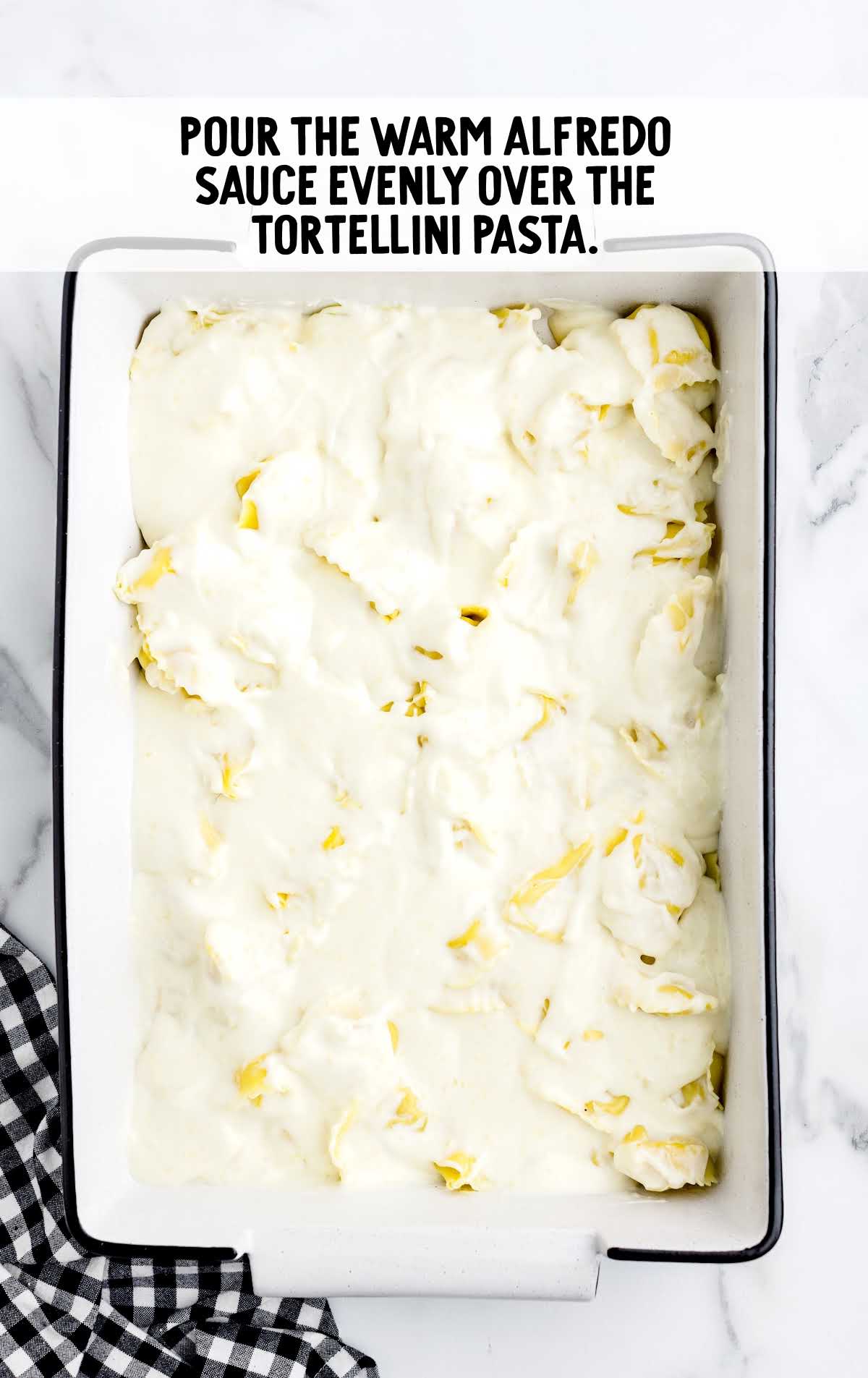 warm alfredo sauce poured over the tortellini pasta in a baking dish