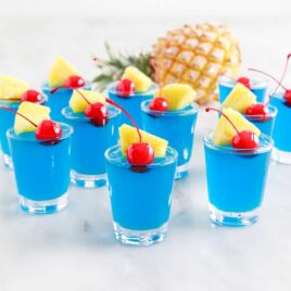 a close up shot of Blue Hawaiian Jello Shots topped with a cherry and slice of pineapple