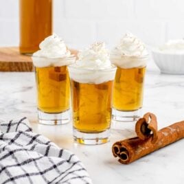 a close up shot of Cinnamon Roll Fireball Shot in cups topped with whipped cream
