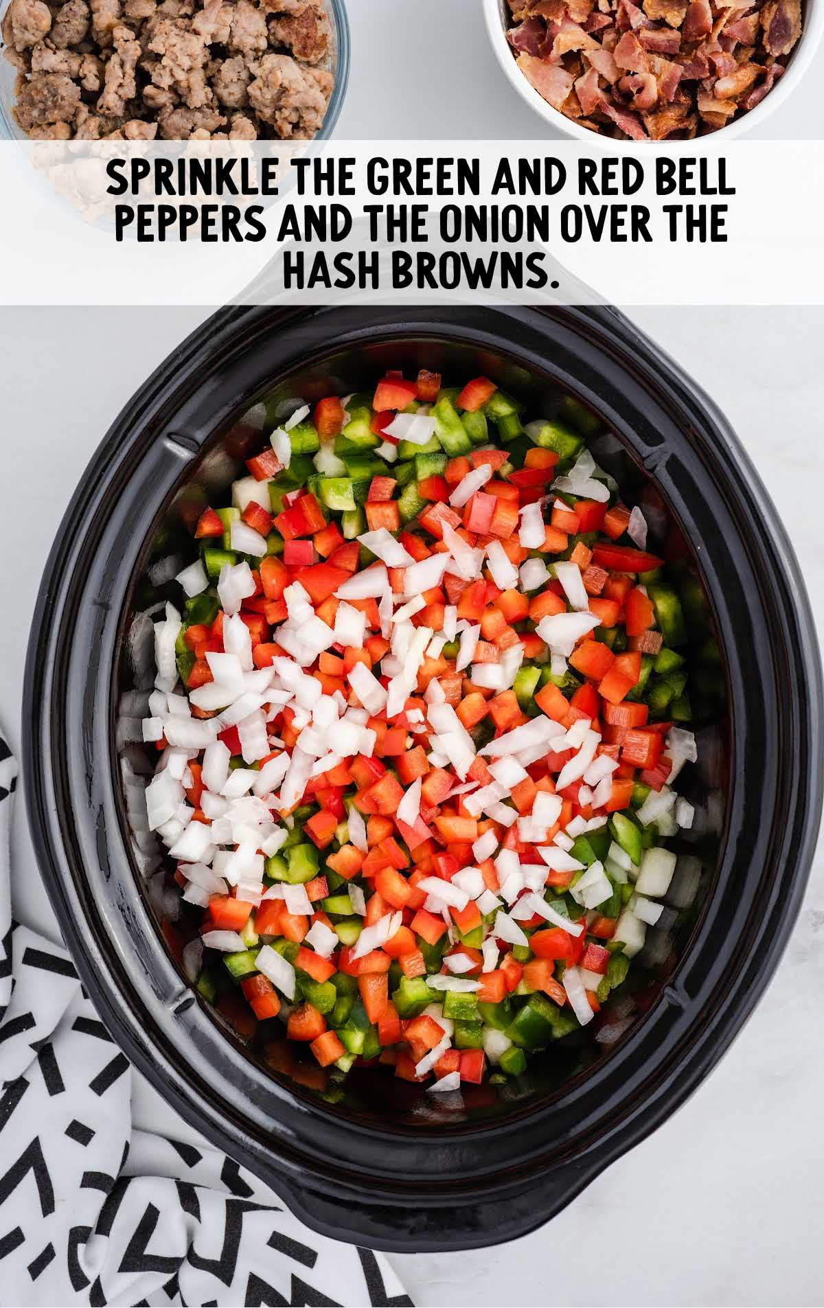 green red bell peppers and onion sprinkled over the hash browns in a crockpot
