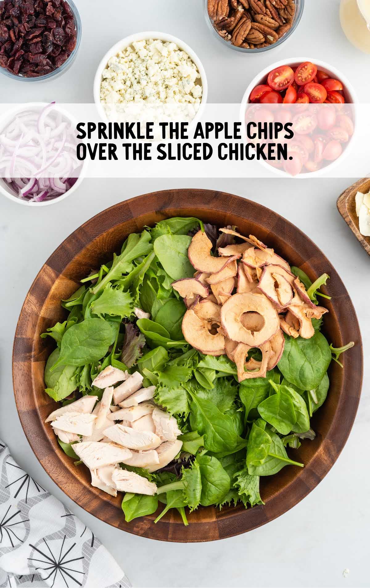apple chips sprinkled over the sliced chicken in a bowl