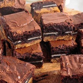 a close up shot of Slutty Brownies on a wooden board with some stacked on top of each other