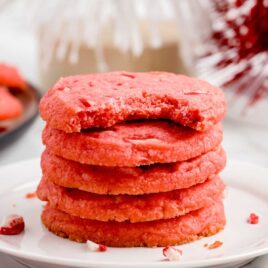 close up shot of Candy Cane Shortbread Cookies stacked on top of each other with one having a bite taken out of it on a plate