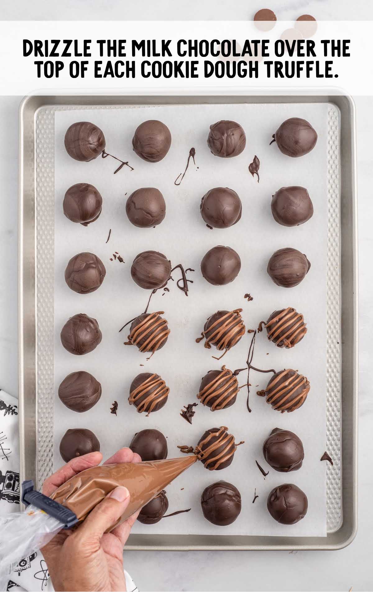 milk chocolate drizzled over the top of each cookie dough truffle on a baking sheet