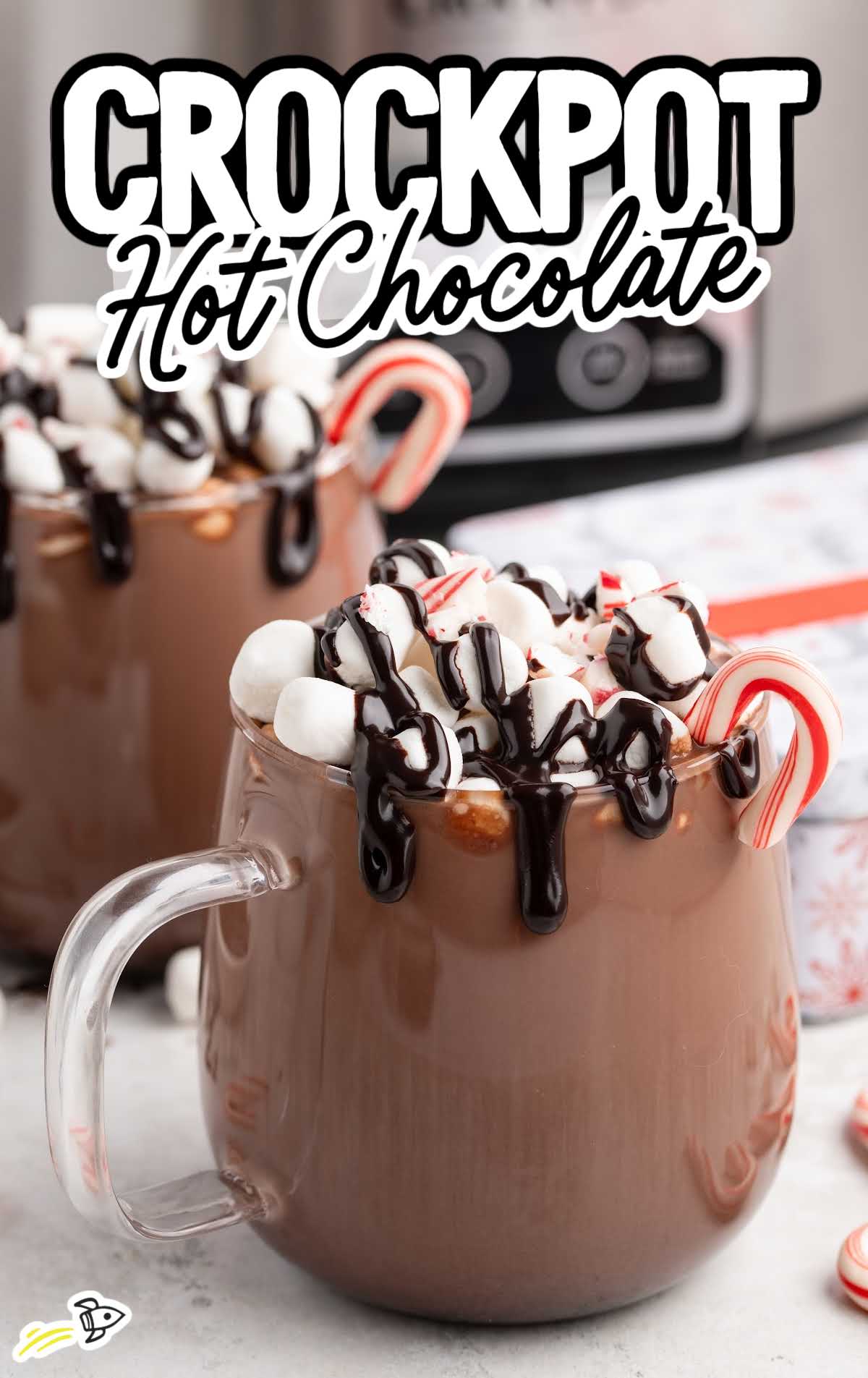 Mug of thick crockpot hot chocolate with whipped cream, marshmallows, chocolate drizzle, and a candy cane garnish.