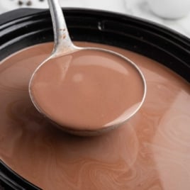 Ladle lifting smooth crockpot hot chocolate from the slow cooker for serving.