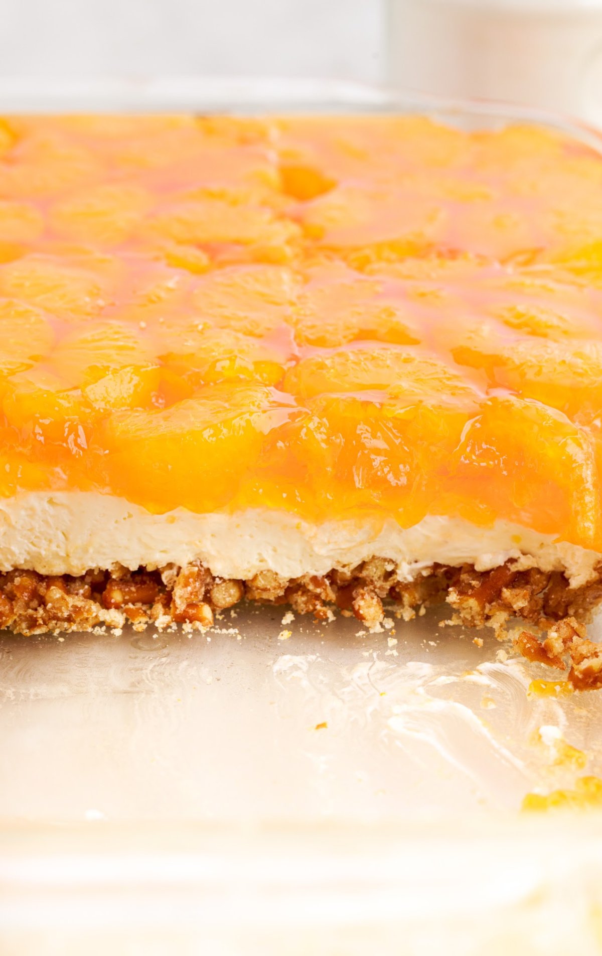 An orange pretzel salad in a glass baking dish, sliced with pieces taken out.