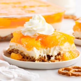 A slice of orange pretzel salad on a plate with a dollop of whipped cream.