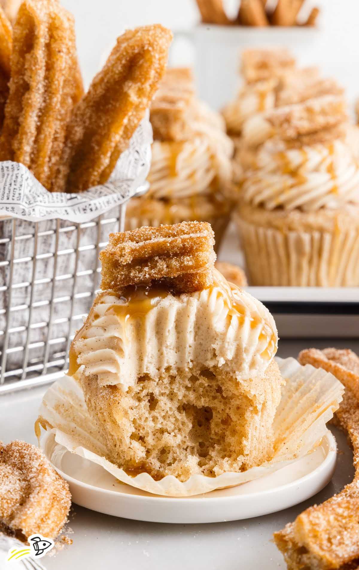 close up shot of a Churro Cupcake with a bite taken out of it on a plate