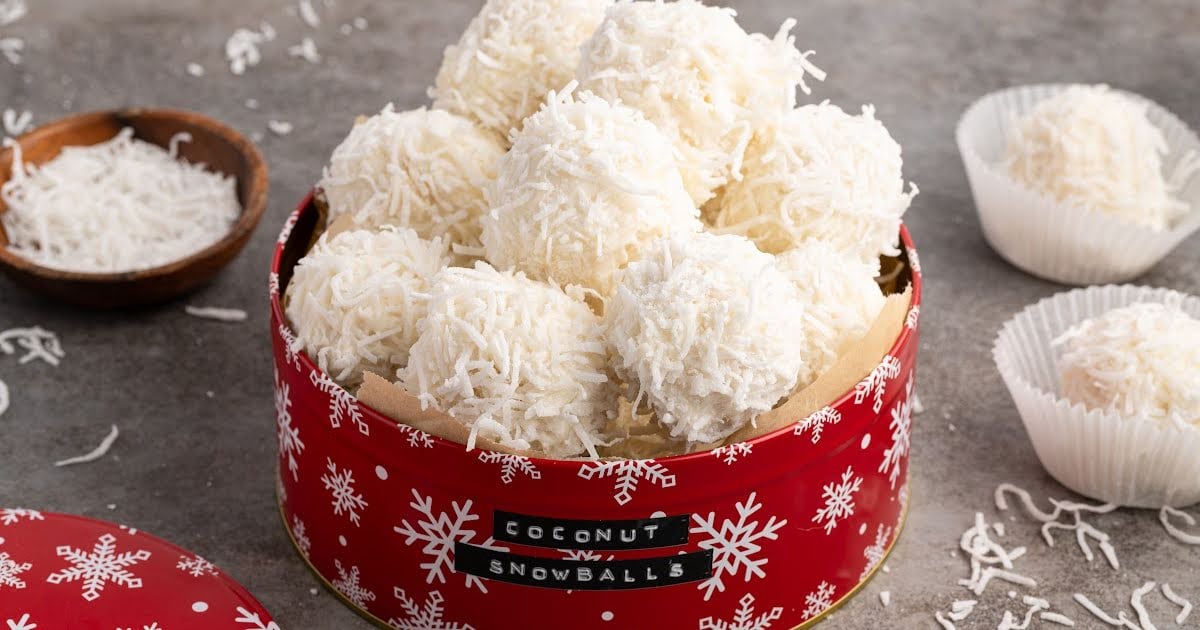 Coconut snowballs arranged in a red snowflake tin for a festive Christmas treat.
