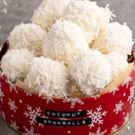 Coconut snowballs arranged in a red snowflake tin for a festive Christmas treat.
