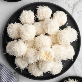 Top-down view of coconut snowballs on a black plate for the recipe card.