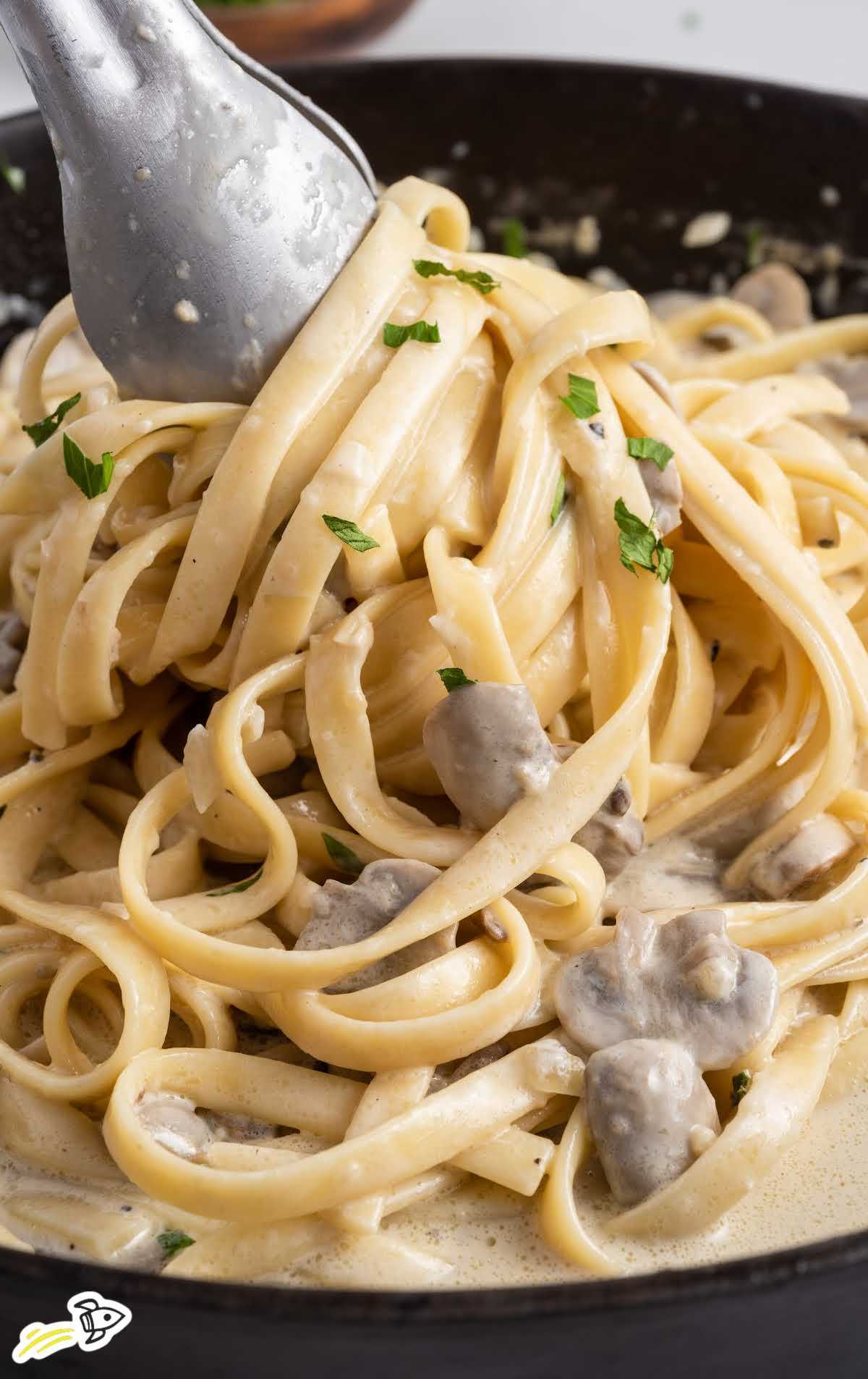 close up shot of Creamy Mushroom Pasta on a skillet with tongs