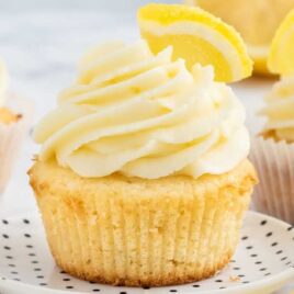 a close up shot of a Lemon Cupcake on a plate topped with a slice of lemon and frosting