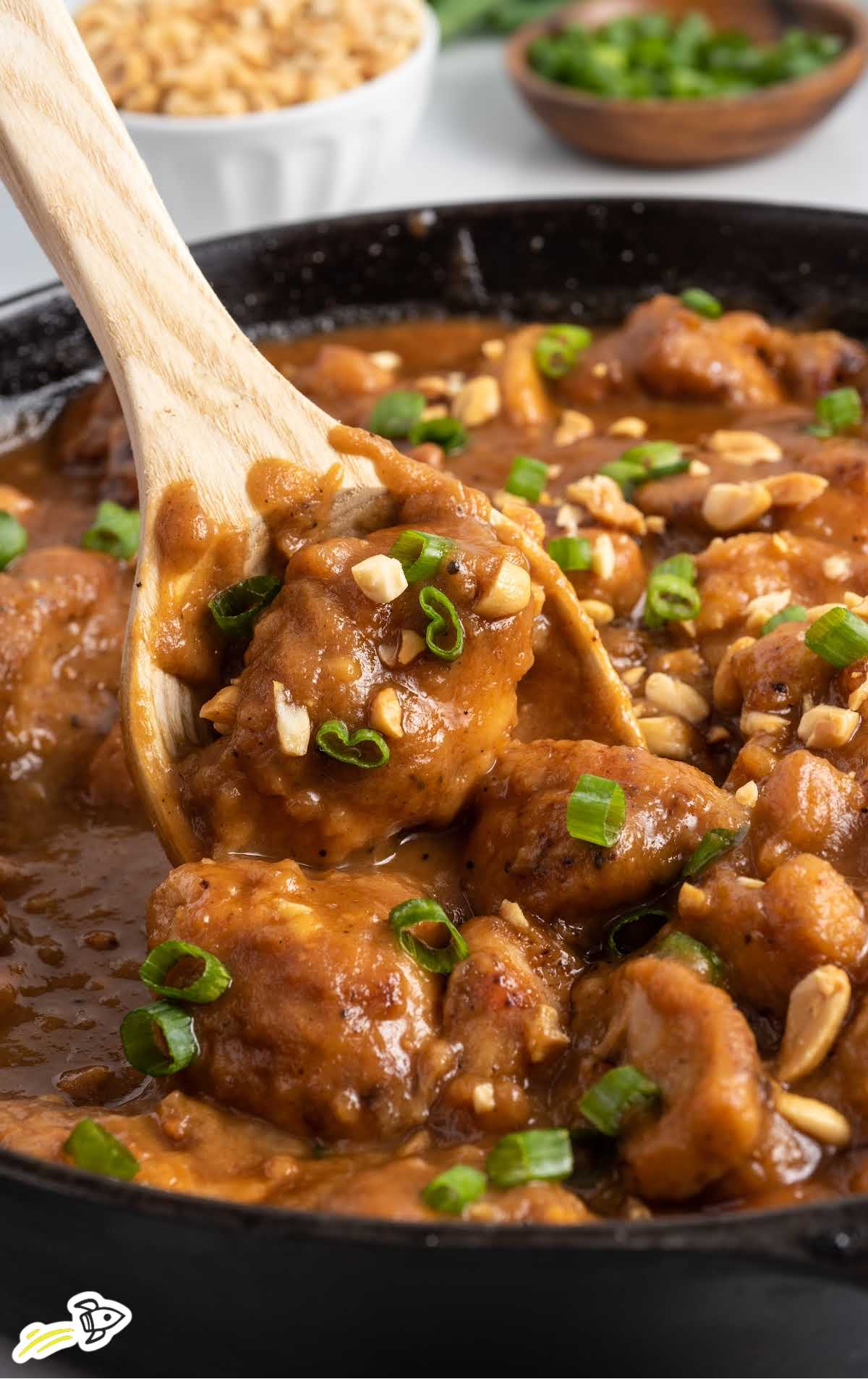 a close up shot of Peanut Butter Chicken in a skillet with a wooden spoon grabbing some