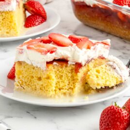 a close up shot of a slice of Strawberry Tres Leches Cake on a plate with a piece taken by a spoon
