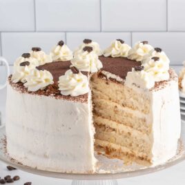 a close up shot of Tiramisu Cake with a slice missing on a cake stand
