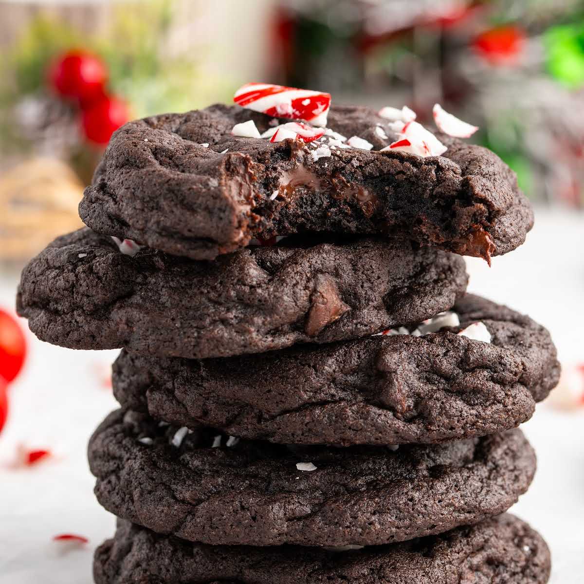 Stack of chewy chocolate peppermint cookies with melted chocolate centers and crushed candy cane topping.