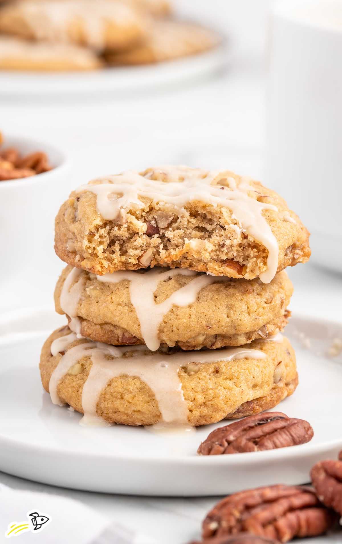 a close up shot of Maple Cookies stacked on top of each other with one having a bite taken out of it on a plate
