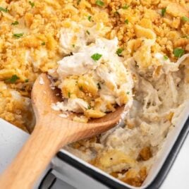 a close up shot of Million Dollar Chicken Casserole with a wooden spoon grabbing a piece