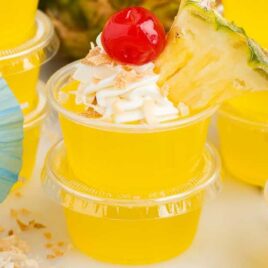 a close up shot of Pina Colada Jello Shots with one topped with a cherry and a slice of pineapple