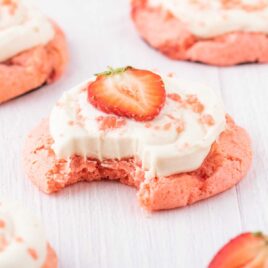a close up shot of a Strawberry Cookie with Cream Cheese Frosting with a bite taken out of it
