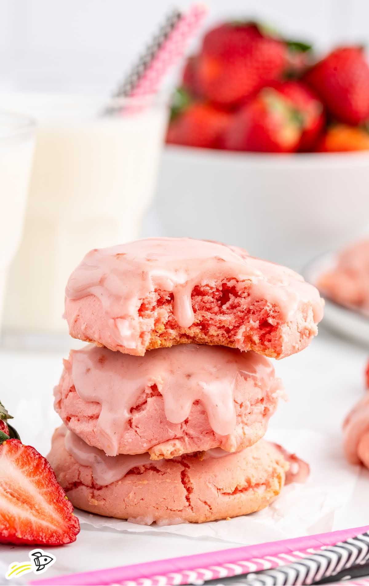 close up shot of Strawberry Sheet Cake Cookies stacked on top of each other with one having a bite taken out of it