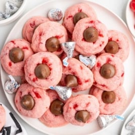 Overhead shot of plate piled with cherry kiss cookies and Hershey’s Kisses scattered around