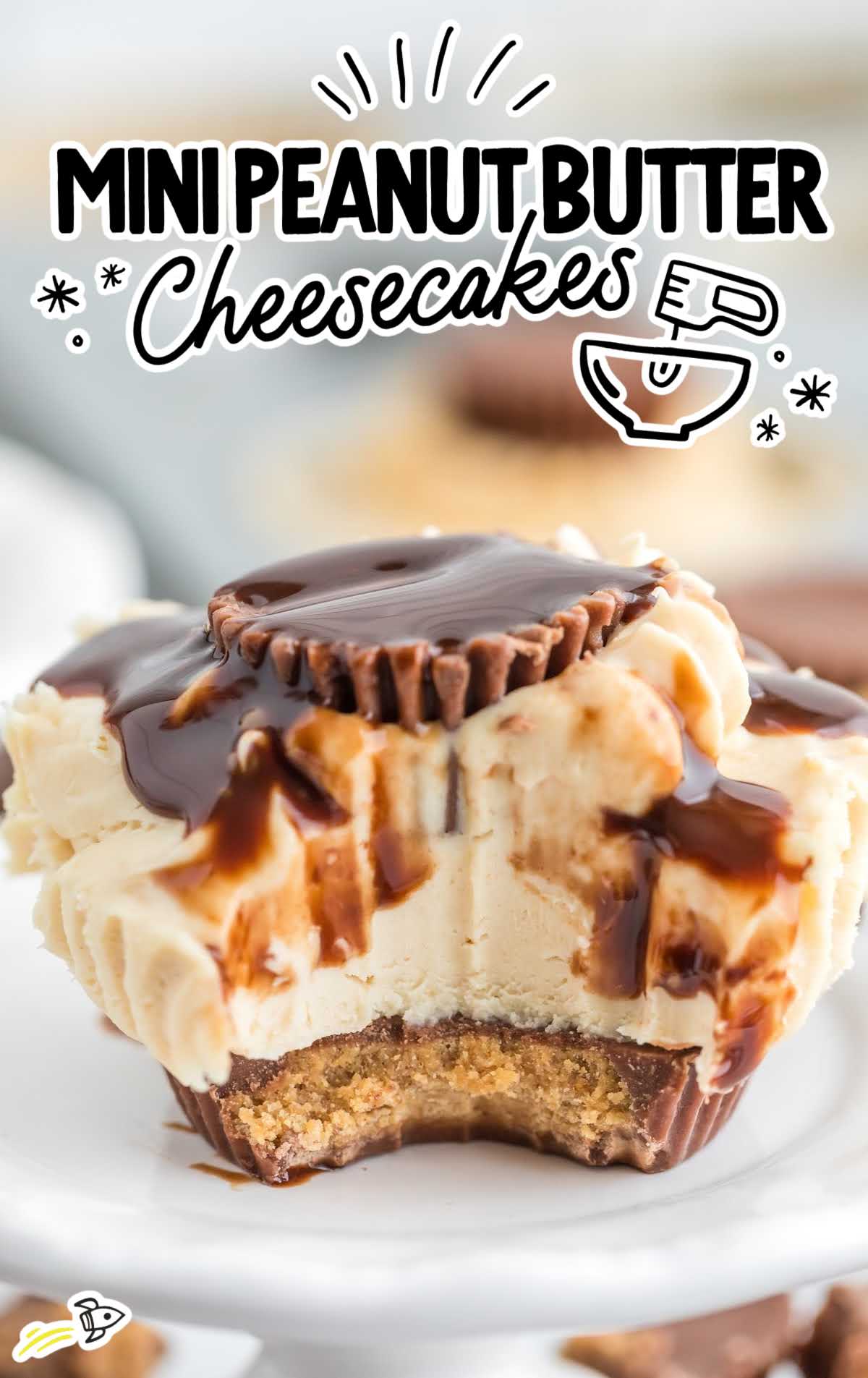 a close up shot of a Mini Peanut Butter Cheesecake drizzled with chocolate sauce and a bite taken out of it