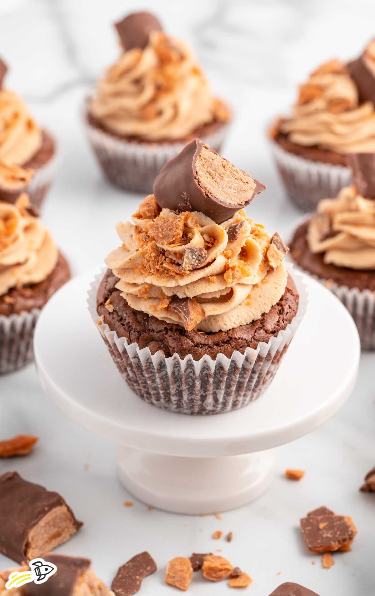 a close up shot of a Butterfinger Cupcake with a bite taken out of it on a cake stand