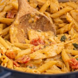 a close up shot of One Pot Chicken Pasta with a piece being picked up by a wooden spoon