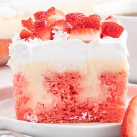 a close up shot of a slice of Strawberry Cheesecake Poke Cake on a cake