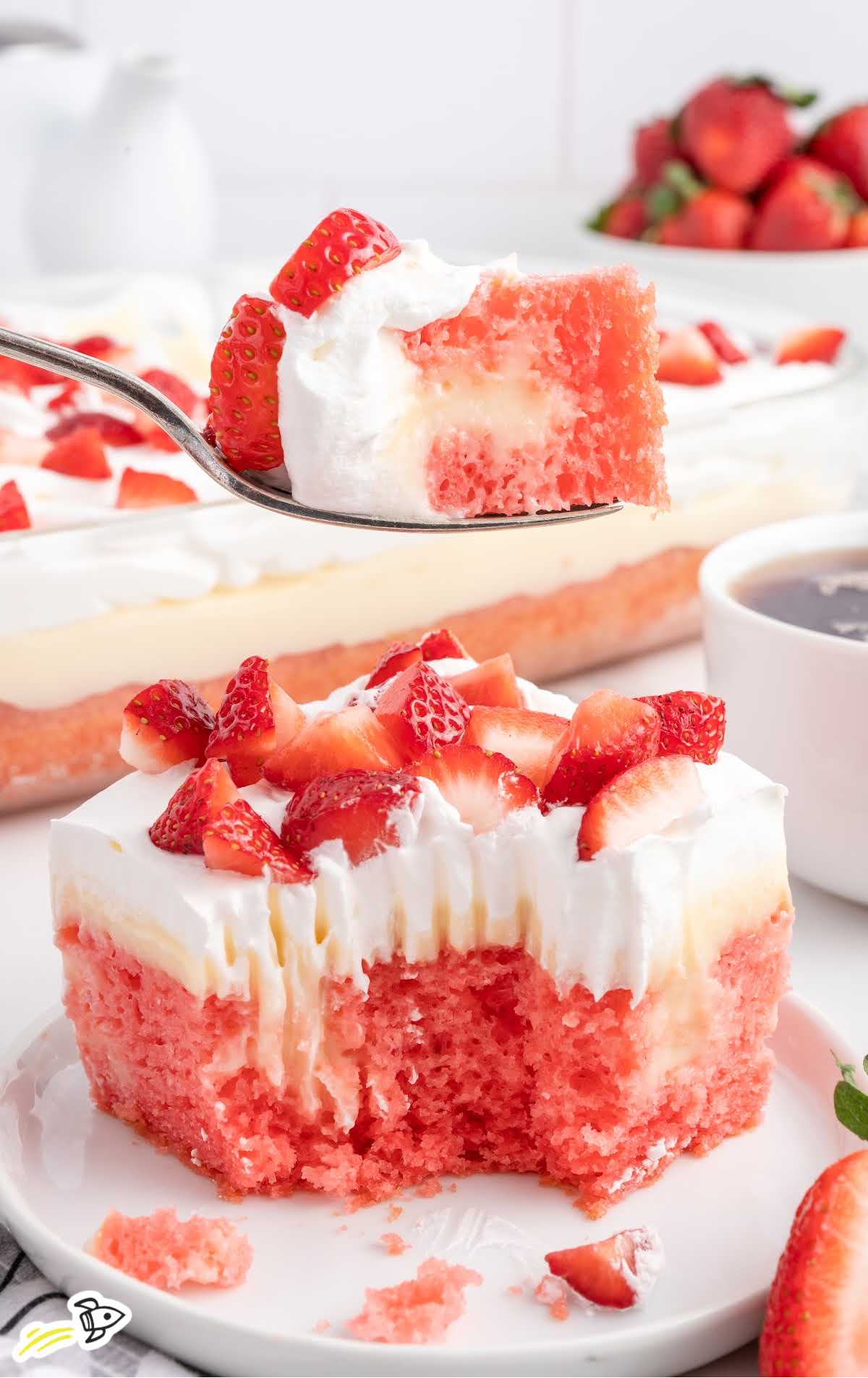 a close up shot of a slice of Strawberry Cheesecake Poke Cake on a cake with a fork grabbing a piece