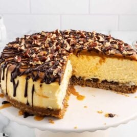 a close up shot of Turtle Cheesecake with a couple of pieces taken out on a cake stand