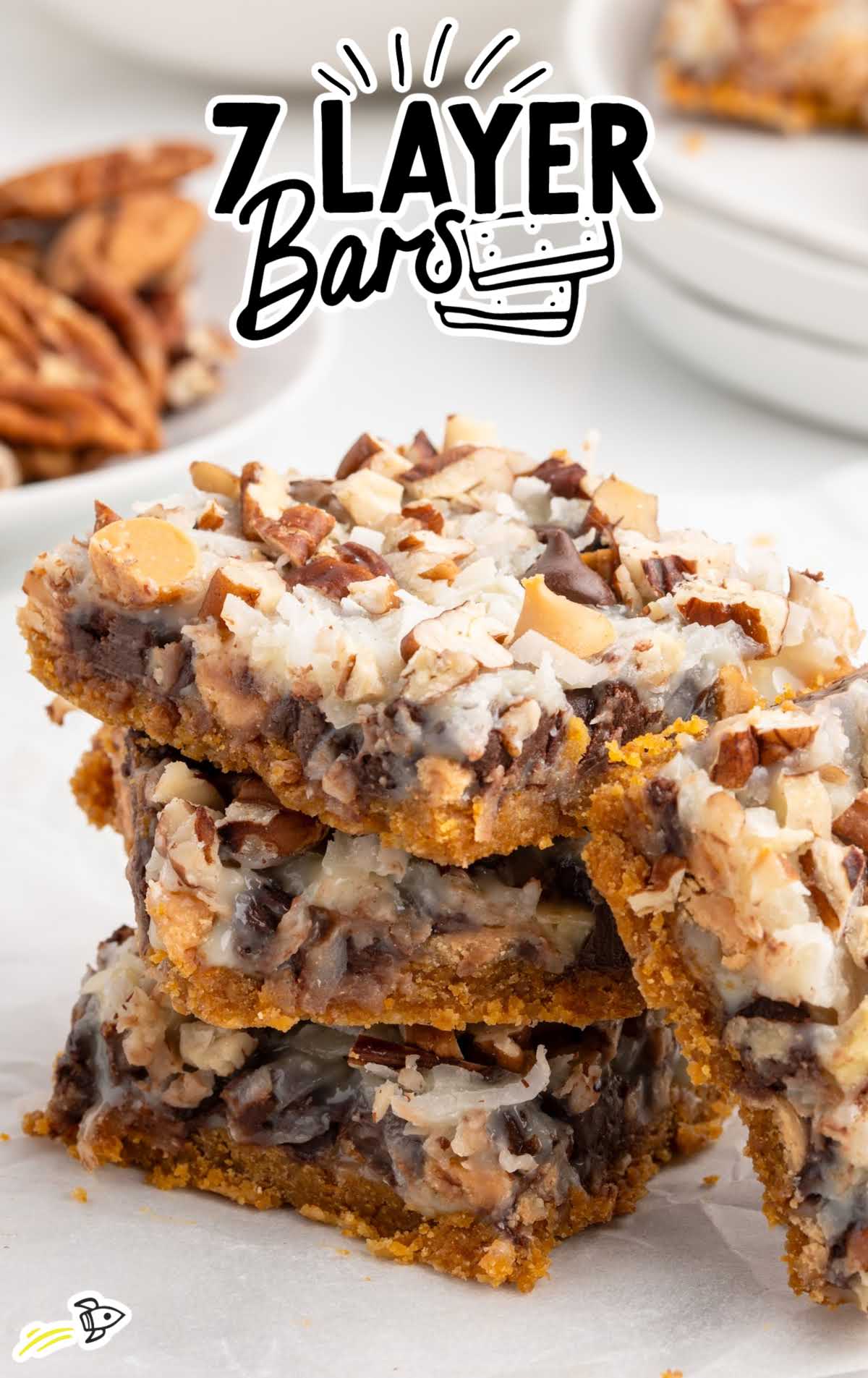 Stack of three 7 layer bars on parchment paper showing the gooey chocolate, coconut, and pecan layers.